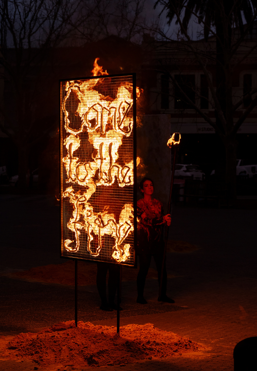 A structural sculpture on fire, the sculpture reads 'Come to the fire'